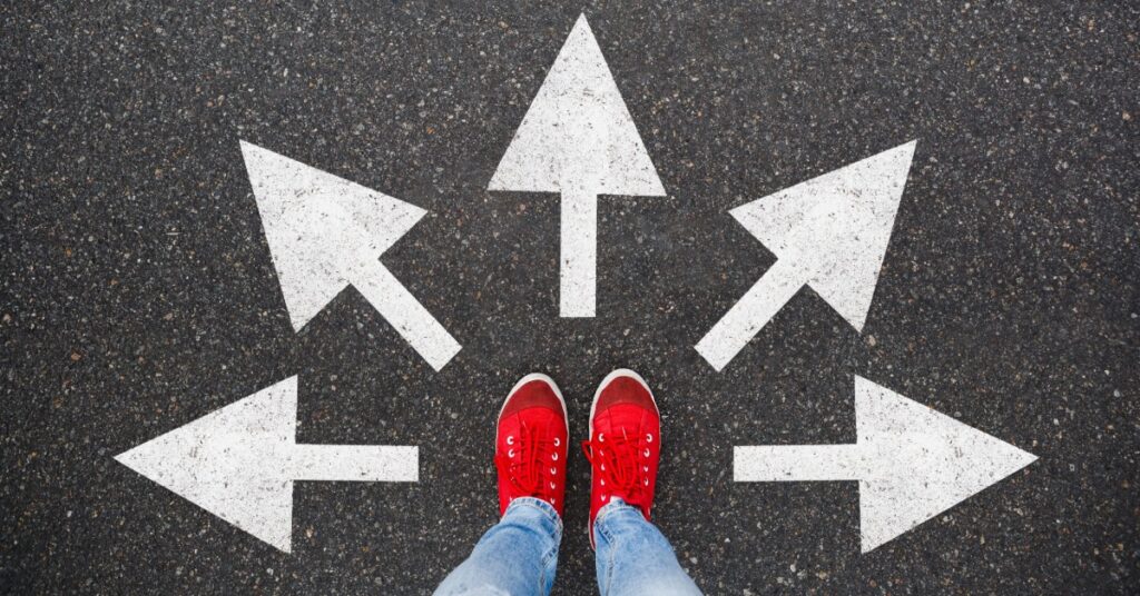 A person wearing red sneakers stands on asphalt marked with white arrows pointing forward, left, right, and diagonally.