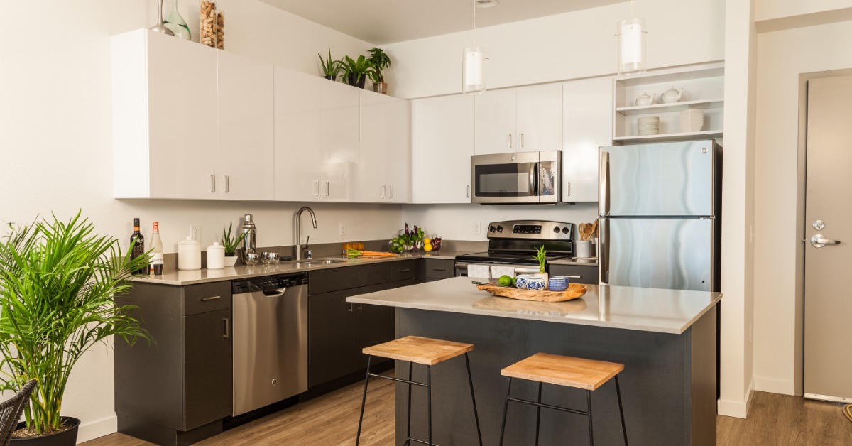 An L-shaped kitchen with a stainless-steel fridge, stove, microwave, and dishwasher. Pendant lights hang over an island.