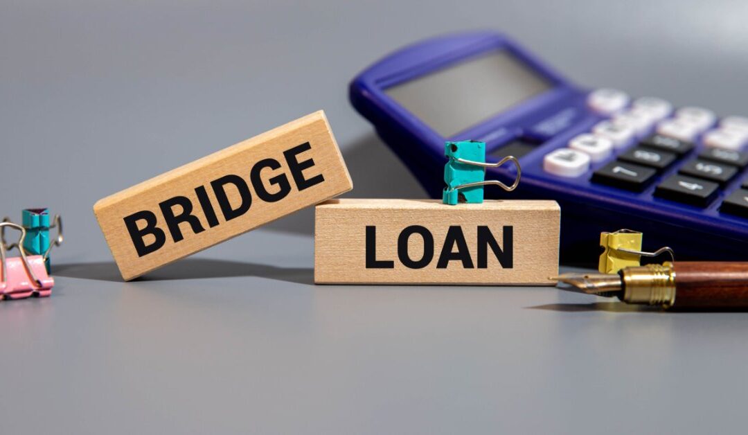 The words “BRIDGE” and “LOAN” are on two wooden blocks near a purple calculator, binder clips, and a fountain pen.