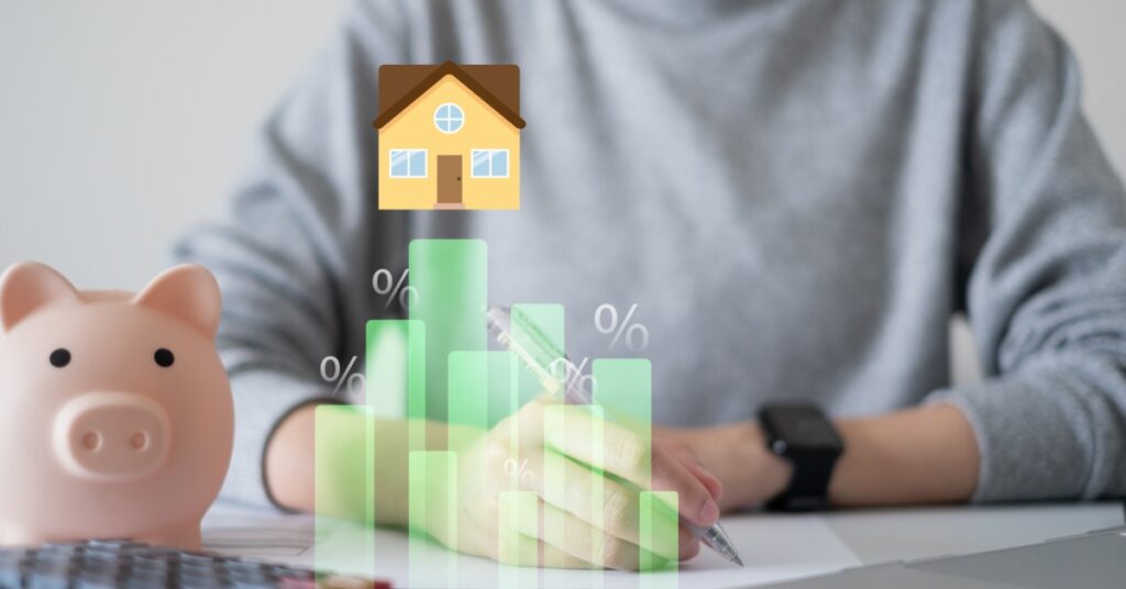 A person writes at a desk with a nearby piggy bank, a calculator, and a transparent bar chart marked with a house icon.