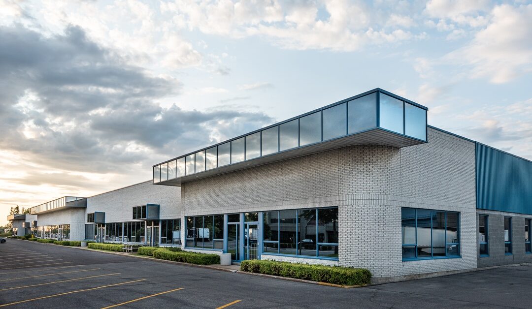 A commercial building has white brick walls, blue metal siding, and reflective windows. The parking lot is empty.