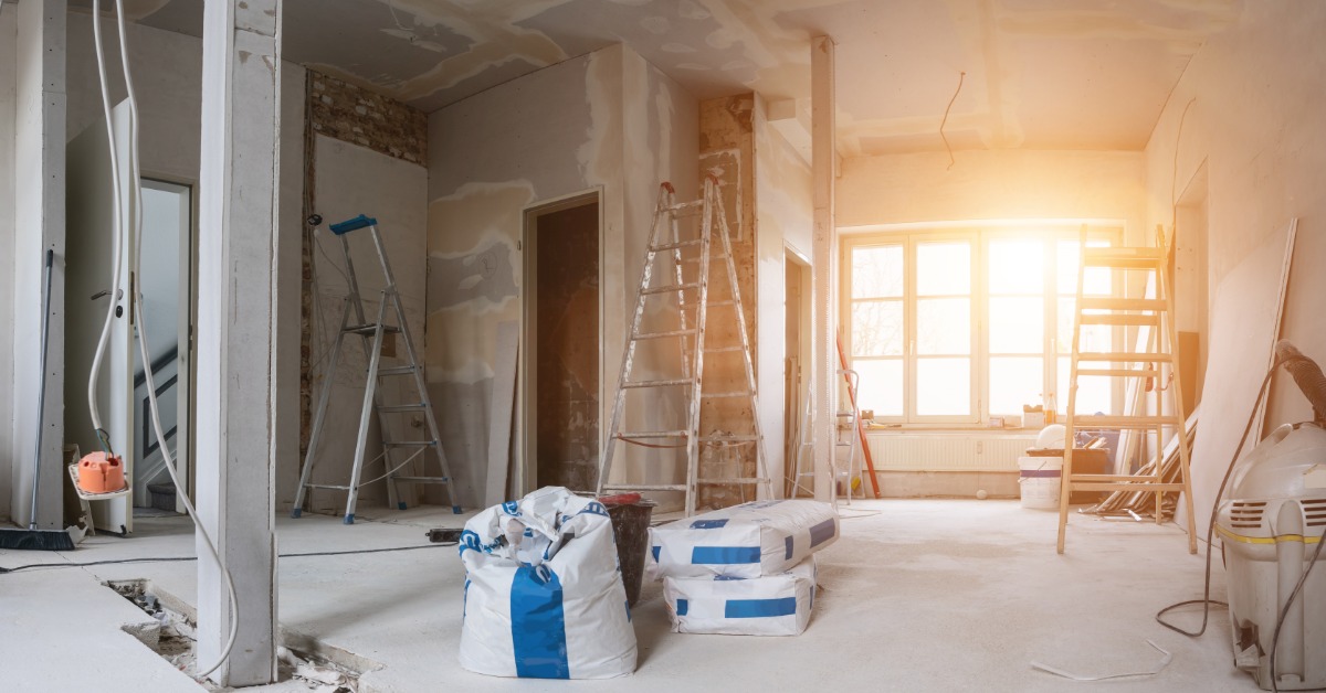 An unfinished interior with exposed wiring and partially finished walls contains several ladders and building materials.