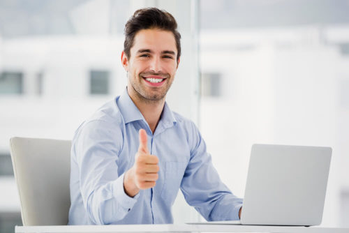 Man smiling and giving a thumbs up while working on a computer